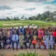 The diverse cohort poses in front of a scenic African camp landscape