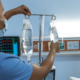 Stock photo. A nurse faces away from the camera as she hangs a bag of liquid on an IV pole at the head of a patient bed.