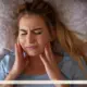 A white, young adult woman clutches her jaw, as someone with a temporomandibular disorder might do.