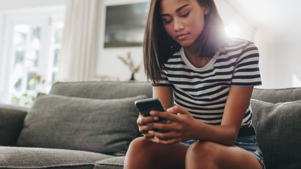 Teenage girl wearing striped shirt sitting on couch and holding phone.
